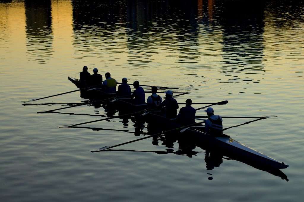 Nine people rowing a long kayak as a team. Differences Between Groups and Teams