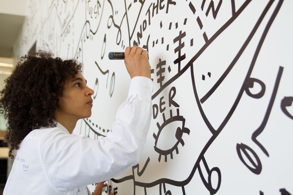 close up of artist shantell martin drawing on a white wall with a black paint pen