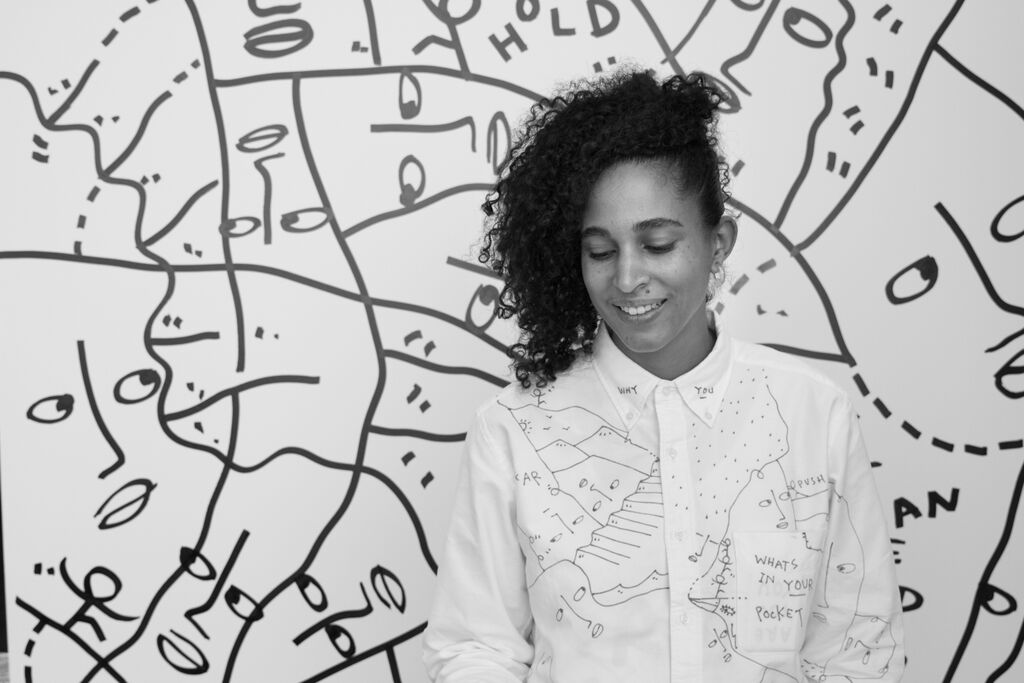 black and white portrait of artist Shantell Martin standing in front of her black and white faces connected as an art piece