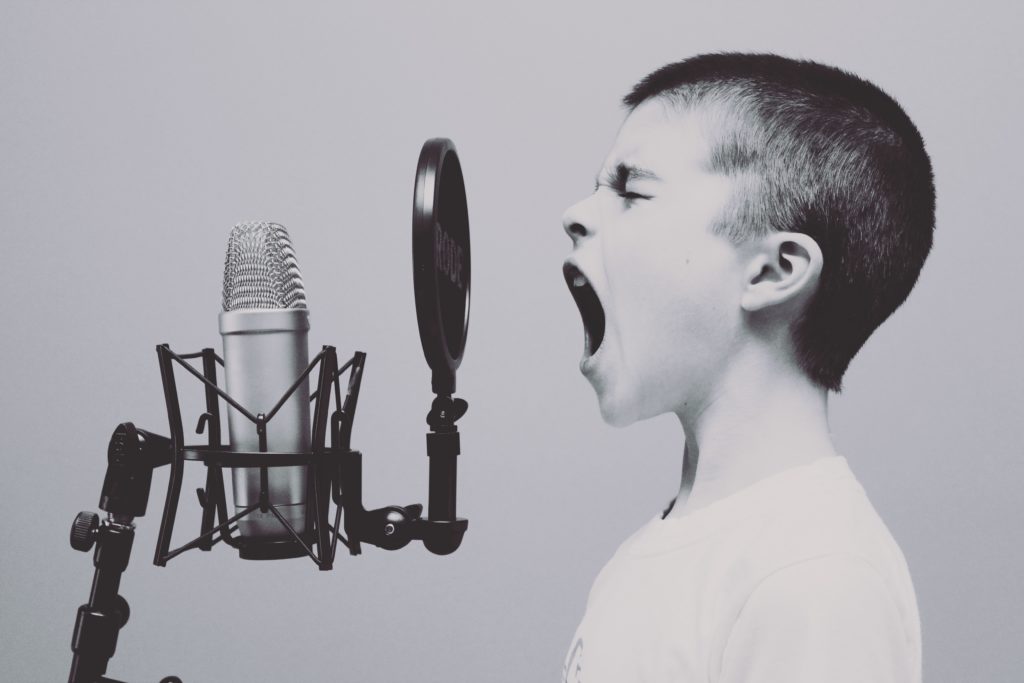 Young boy speaking loudly into a microphone. Marketers have the passion to make a difference.