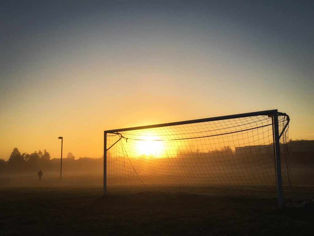 The sun peeks over the horizon behind the silhouette of a soccer goal on a foggy morning. Learn about the personality characteristics of the best athletes, coaches, and teams.