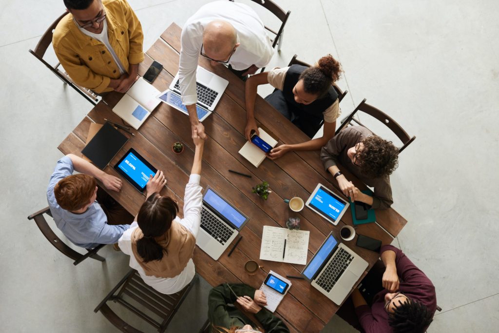 A group of employees and leaders sit around a conference table using laptops to discuss leadership development initiatives.