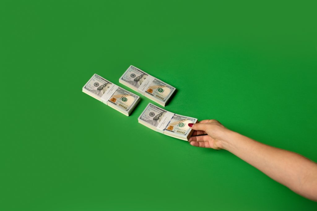 Signifying the cost of bad hires, three banded stacks of money lie horizontally in a triangle against a green backdrop.