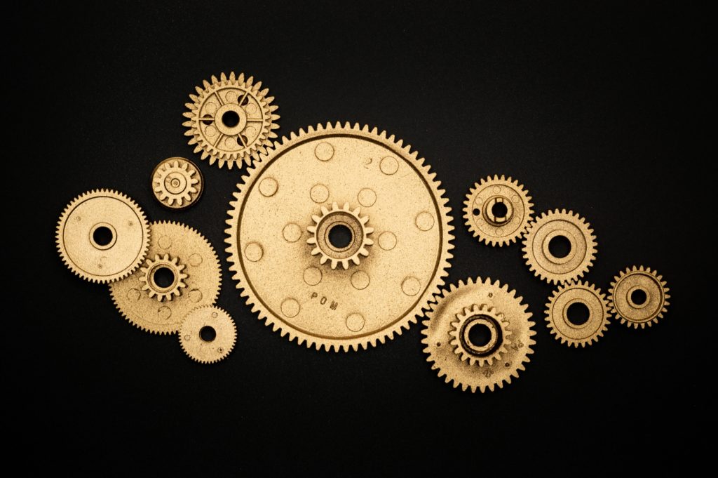 Signifying team trust, an array of golden cogs, some overlapping and some distanced, are displayed against a black background. 