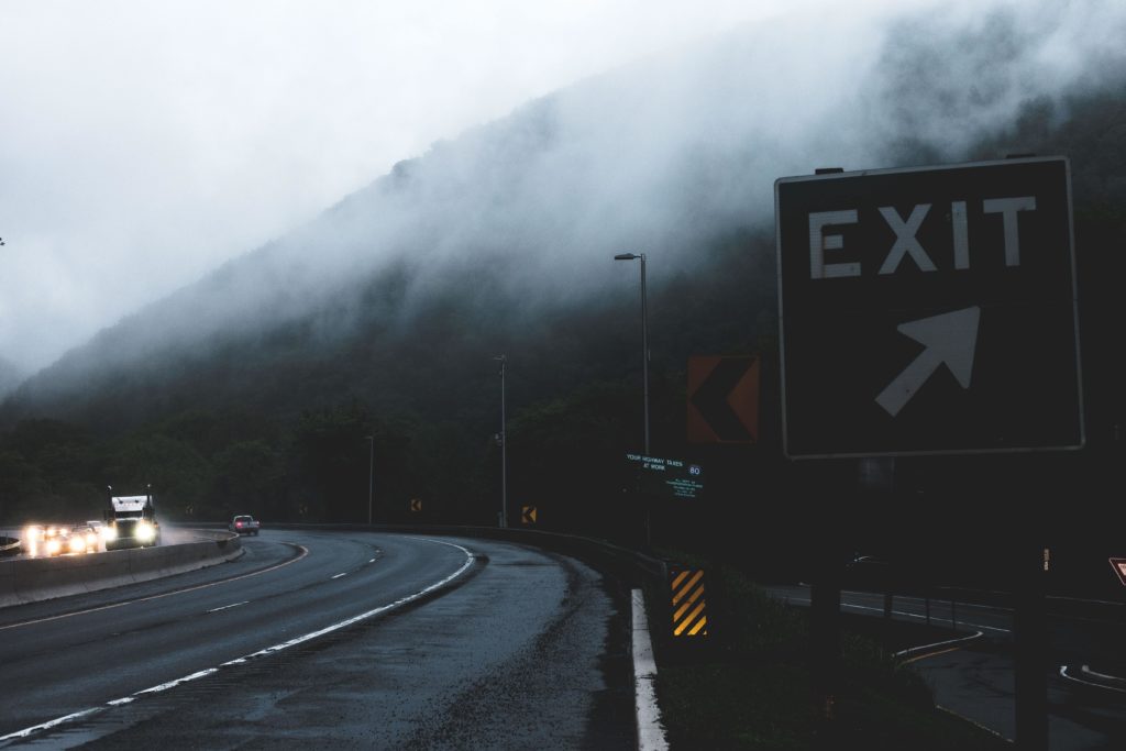 Why are so many people quitting their jobs? In this photo, a green exit sign alongside a foggy, winding highway signifies the question of what might be causing the so-called Big Quit or Great Resignation.