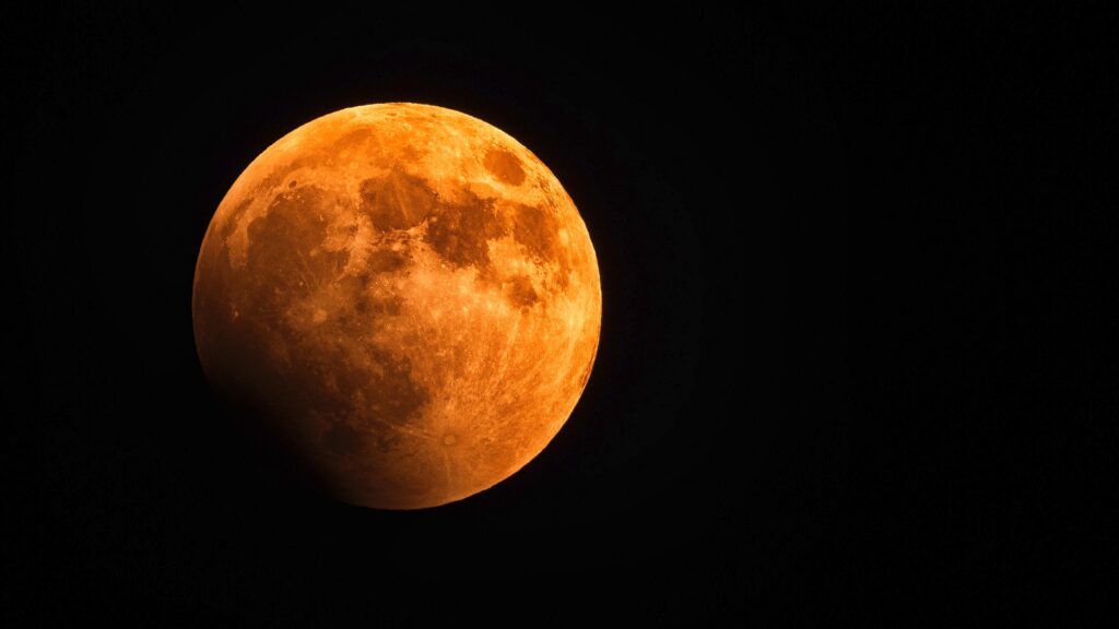 A blood moon is positioned against a black backdrop. Belief in the occurrence of particular events during a full moon is one of the paranormal psychology concepts discussed in this blog.