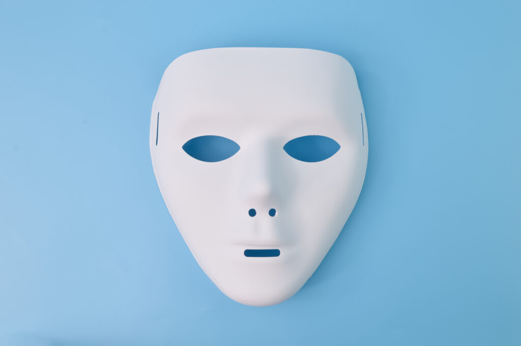 A white face mask with eye, nostril, and mouth holes rests on a powder blue background. The mask photo accompanies a blog post about self-deception and evolutionary theory.