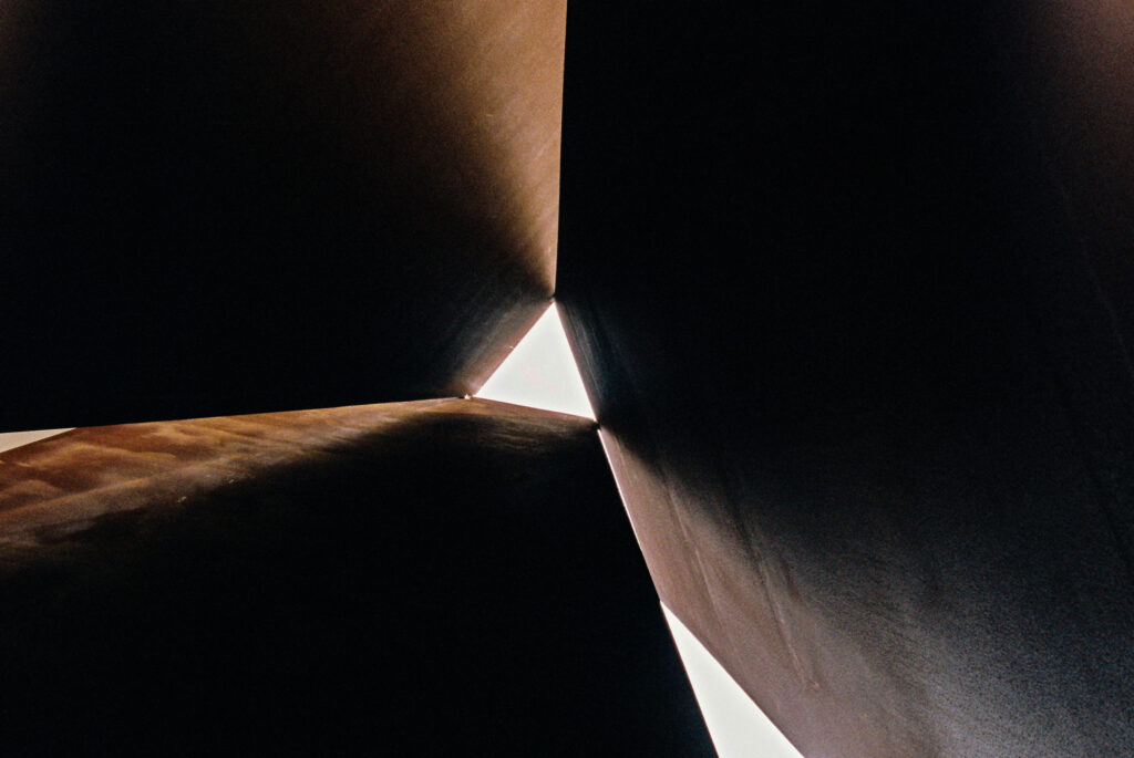 A photo, taken from an upward perspective, of three adjacent boulders. Where the tops of the boulders meet, a triangle of sunlight peeks through. Because the boulders are otherwise blocking the sun, they appear dark. The photo accompanies a blog post about the Dark Triad and dark-side personality characteristics.