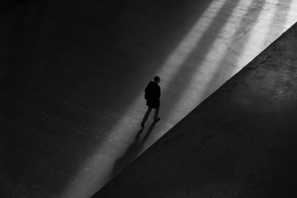 This photo shows a bird’s-eye view of a silhouette walking across a terrace. The person is walking in a sliver of light amid shadows. The photo signifies Carl Jung’s shadow archetype and accompanies an article about why Jung matters to personality psychology.