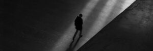 This photo shows a bird’s-eye view of a silhouette walking across a terrace. The person is walking in a sliver of light amid shadows. The photo signifies Carl Jung’s shadow archetype and accompanies an article about why Jung matters to personality psychology.