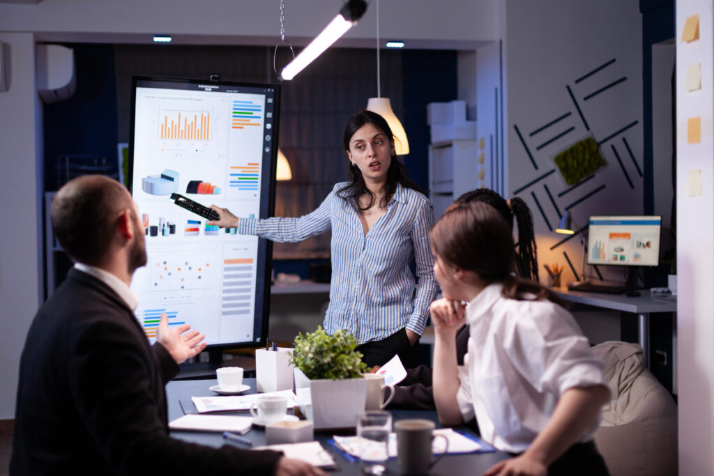 A leader gestures at a large monitor showing business data. The other professionals around the conference table are rapt, and the presentation appears to be occurring after hours, as if there is a crisis to respond to. The image accompanies a blog post about strategic leadership in VUCA environments. 