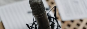 A close-up photograph of a studio microphone. In the background, which is out of focus, scattered papers lie across a tabletop. The image accompanies a blog post about the top five episodes of the Science of Personality podcast from its first three years.
