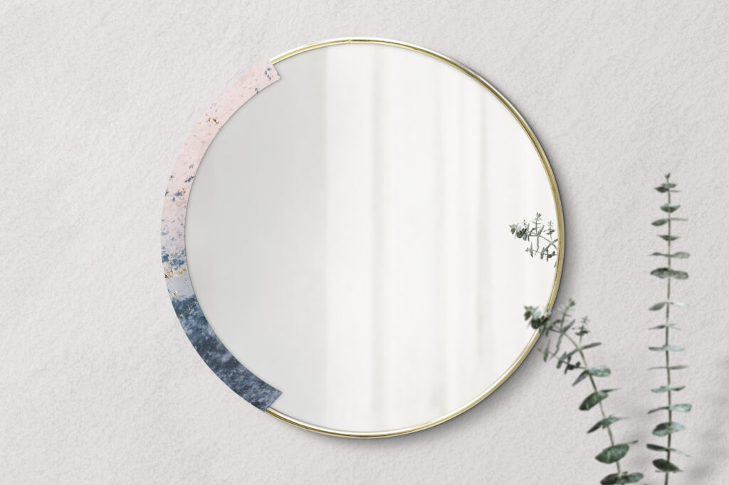 A marble-framed mirror hangs on a beige wall. Next to it is a plant cutting in a vase. No human reflection is visible in the mirror. The photo accompanies a blog post about the psychology of humility.