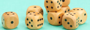 Wooden gaming dice with black markings rest against a robin's-egg blue background. The image accompanies a blog post about how a world without assessments would mean talent decisions are made randomly, as if decision-makers were rolling the dice on candidates.