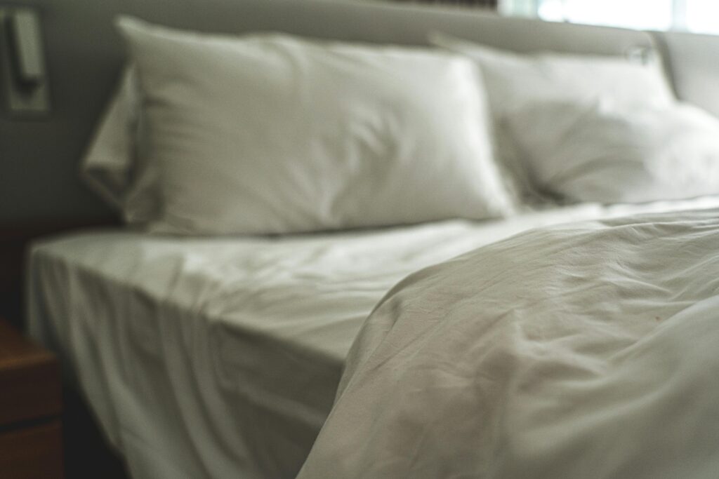 A close-up photograph of an unmade bed dressed with white bedding in dim lighting. The photo is slightly out of focus. It accompanies a blog post about the psychology of sleep, which discusses the relationship between sleep and personality and offers tips on how to improve sleep.