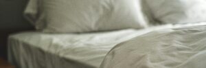 A close-up photograph of an unmade bed dressed with white bedding in dim lighting. The photo is slightly out of focus. It accompanies a blog post about the psychology of sleep, which discusses the relationship between sleep and personality and offers tips on how to improve sleep.