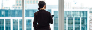 Young Asian businesswoman with digital tablet, standing against office window with city view