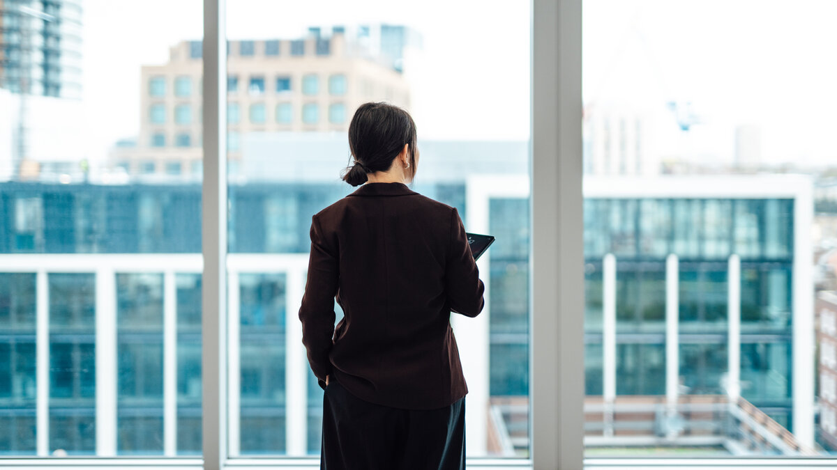Young Asian businesswoman with digital tablet, standing against office window with city view