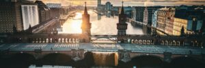 The Oberbaum Bridge spans the Spree River in the center of Berlin, Germany. Sunset light reflects off the surface of the water and illuminates buildings in both traditional and modern architectural styles along the river’s edge. The image accompanies an article spotlighting Hogan data on emergent German leaders.