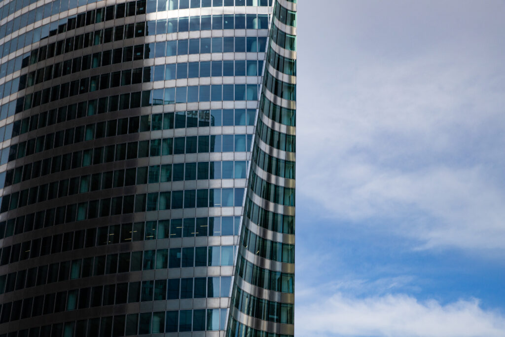 A glass skyscraper reflects the ominous shadow of another skyscraper, which is out of frame. The image accompanies an article about how the dark side of leadership tends to manifest in executives.