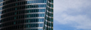A glass skyscraper reflects the ominous shadow of another skyscraper, which is out of frame. The image accompanies an article about how the dark side of leadership tends to manifest in executives.