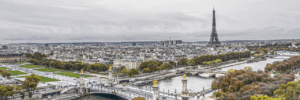 An aerial view of Paris shows the ornate Pont Alexandre III spanning the Seine River, the Eiffel Tower starkly visible against a cloudy sky, and autumn foliage along the riverbanks. The image accompanies an article about aesthetics and agility as personality trends among French executives.