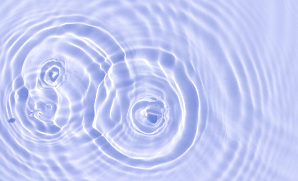 Water or another transparent liquid ripples in three overlapping sets of concentric circles, signifying the ripple effect of creating a coaching culture in an organization. The image is tinted periwinkle. 