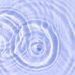 Water or another transparent liquid ripples in three overlapping sets of concentric circles, signifying the ripple effect of creating a coaching culture in an organization. The image is tinted periwinkle.