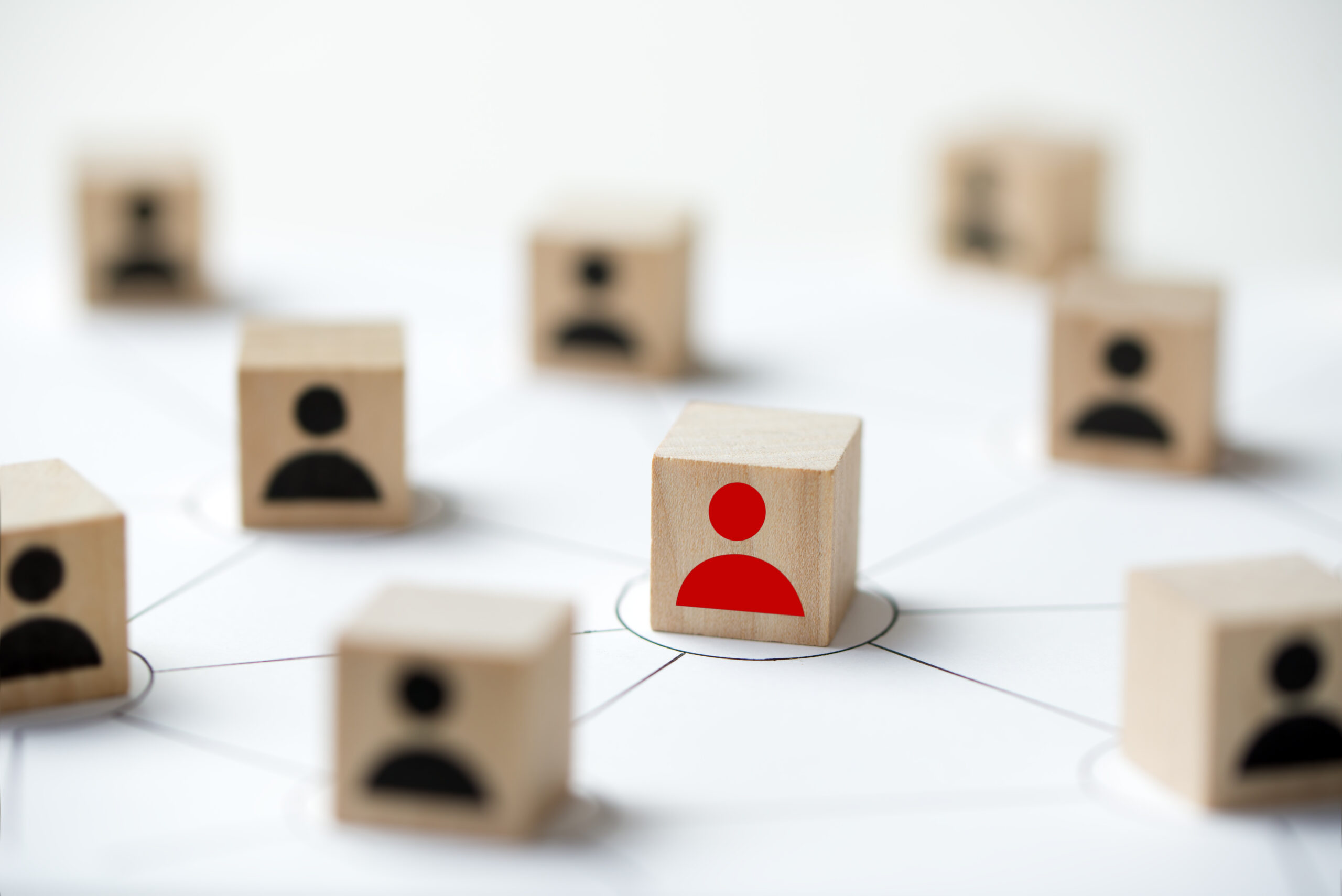 This leadership selection visual metaphor depicts wooden blocks arranged in a network pattern with one red silhouette standing out among black silhouettes. It accompanies an article about new requirements for executive assessment for federal agencies.