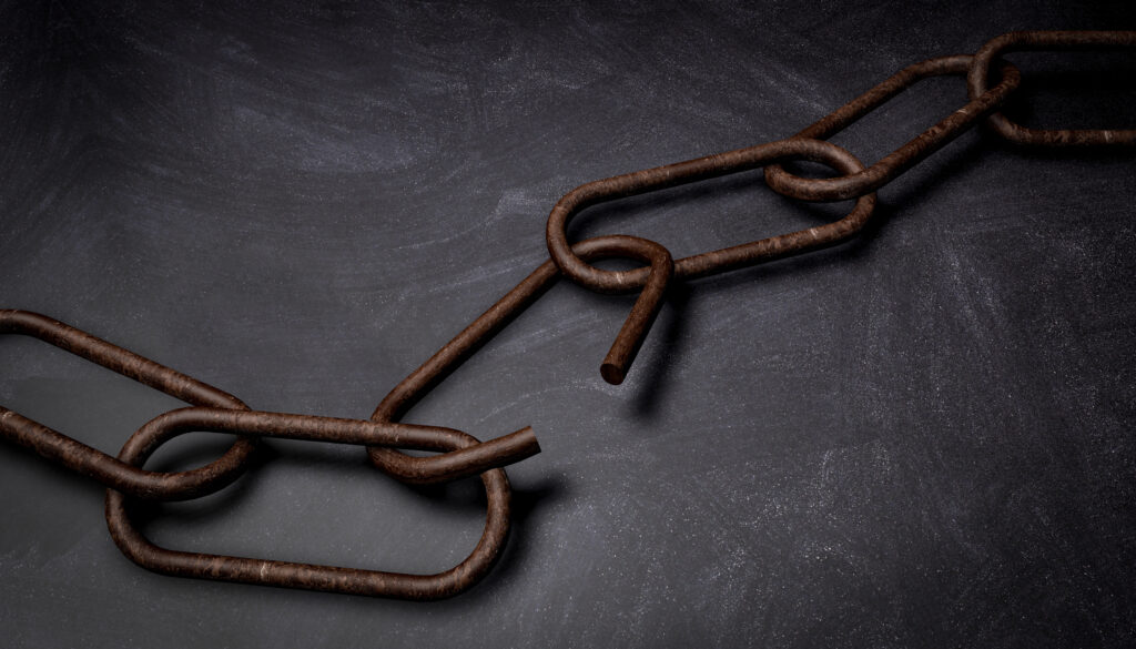 Rusty chain with broken links on a dark surface, illustrating how one weak link compromises the entire chain, as in the case of disengaged employees. The image accompanies an article about workplace freeloaders.