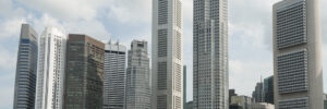 The Singapore Central Business District skyline rises behind the Singapore River, with modern skyscrapers towering over historic shops along the waterfront. The image accompanies an article about emergent Singaporean leaders.