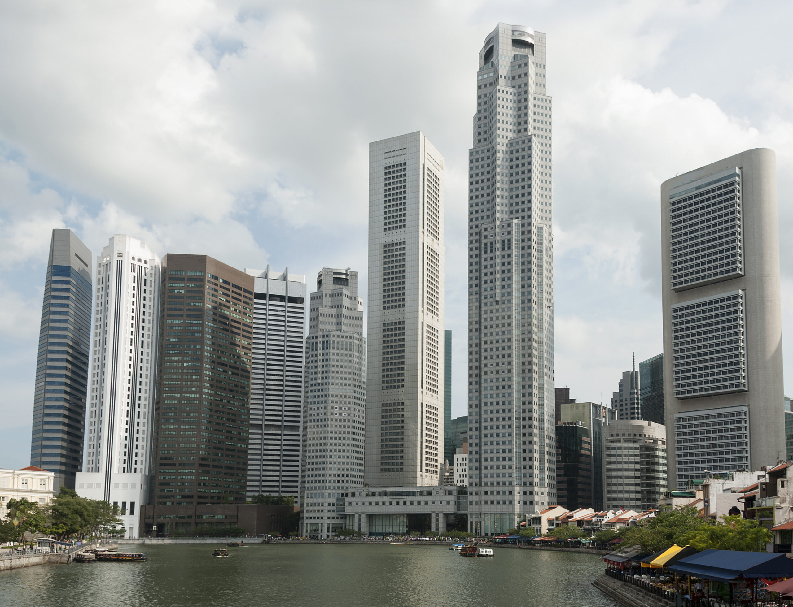 The Singapore Central Business District skyline rises behind the Singapore River, with modern skyscrapers towering over historic shops along the waterfront. The image accompanies an article about emergent Singaporean leaders.