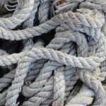 A tangle of thick, weathered light gray rope lies in coils and loops, with visible fraying throughout and several sections showing discoloration from wear. The image accompanies an article about people-pleasing at work.
